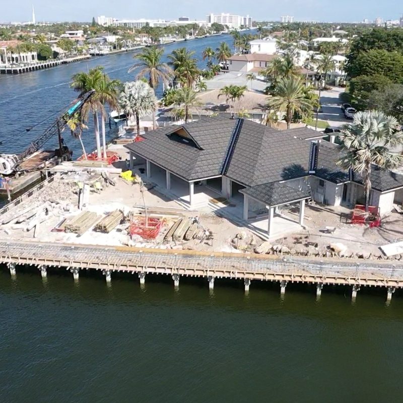 A luxurious waterfront home in Fort Lauderdale with a pool, palm trees, and a clear blue sky.